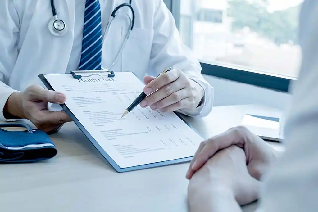Profissional de saúde com jaleco e prancheta Health Check conversando com pessoa assistida em consulta